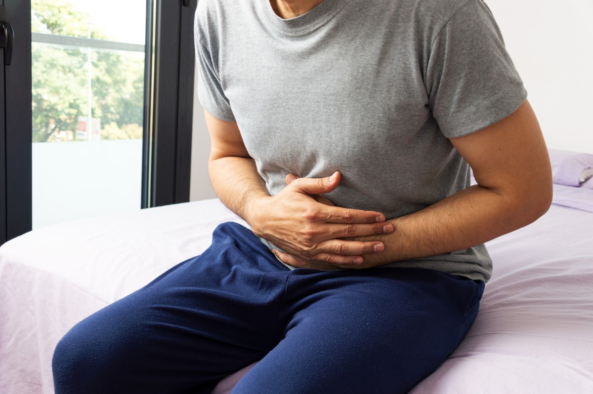 L'uomo ha male allo stomaco, se lo tiene con le mani. È seduto sul letto in pigiama.