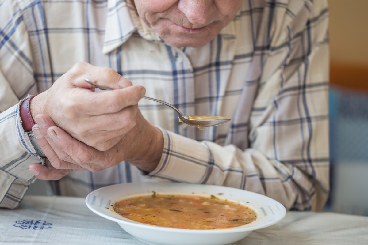 Un uomo mangia una zuppa e tiene la mano contro i tremori del morbo di Parkinson