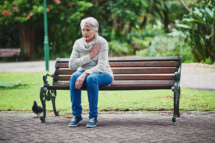 Una donna anziana è seduta su una panchina e accusa problemi cardiaci.