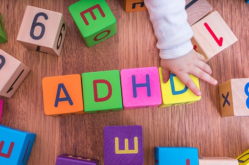 cubetti di lettere per bambini, disposti in modo da formare il nome ADHD, con la mano del bambino