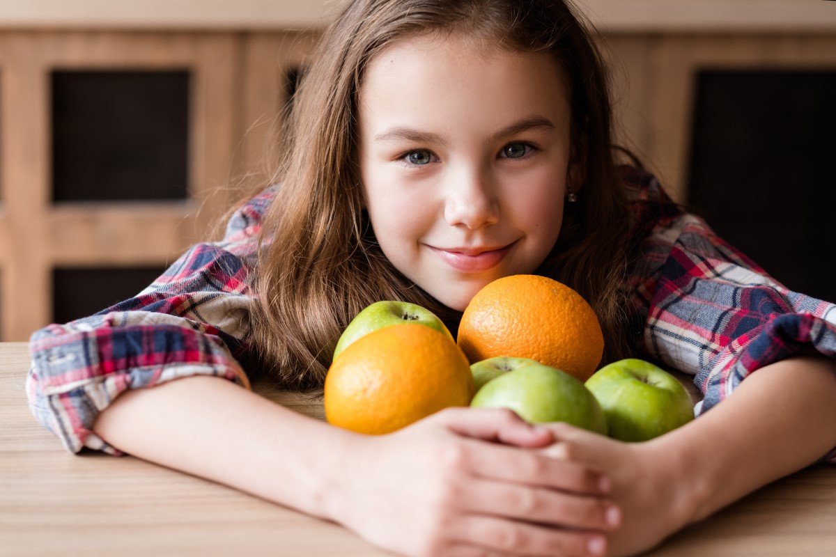 Vitamina C, nella frutta, un bambino che tiene in braccio arance e mele