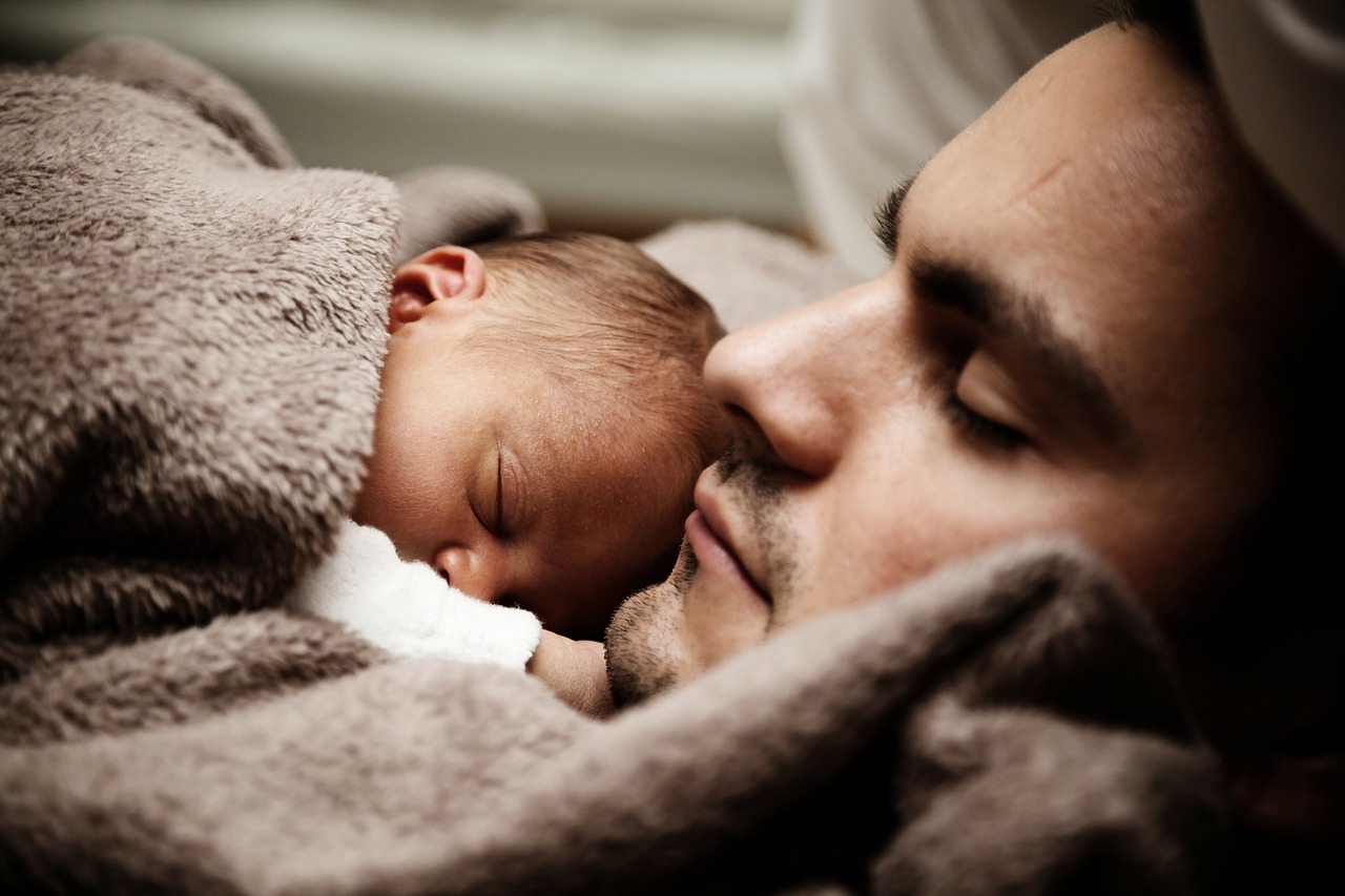 il bambino dorme accanto al padre sotto una coperta marrone