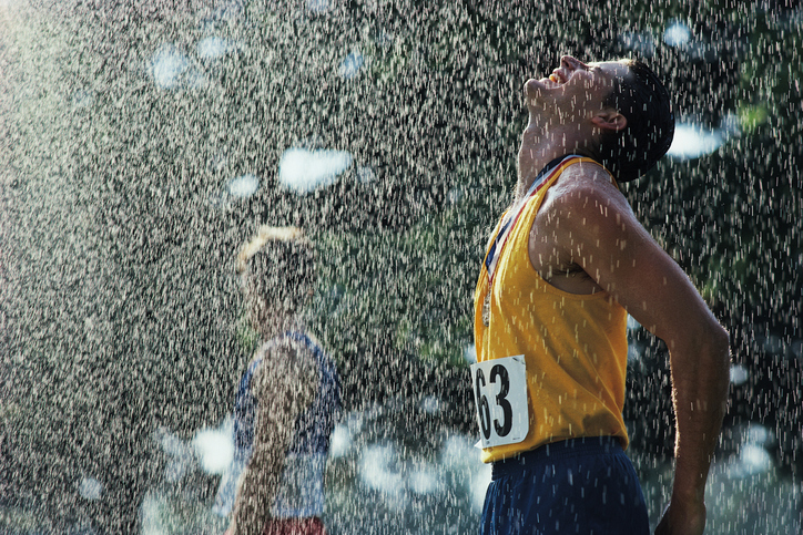 Un atleta dopo aver tagliato il traguardo. Piove. La sua testa è rivolta verso l'alto contro le gocce che cadono. Ha gli occhi chiusi, una medaglia al collo. Indossa una canottiera gialla con il numero 63 e pantaloncini blu.