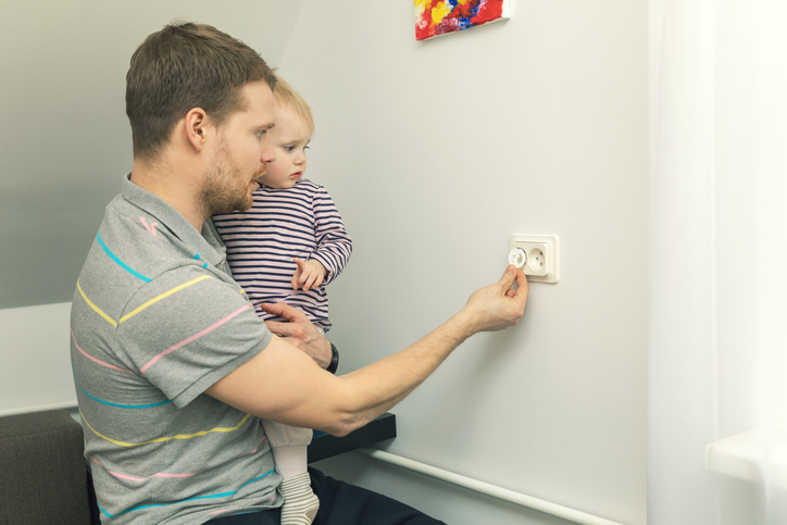 Il papà tiene in braccio un bambino piccolo e chiude la spina con una presa elettrica