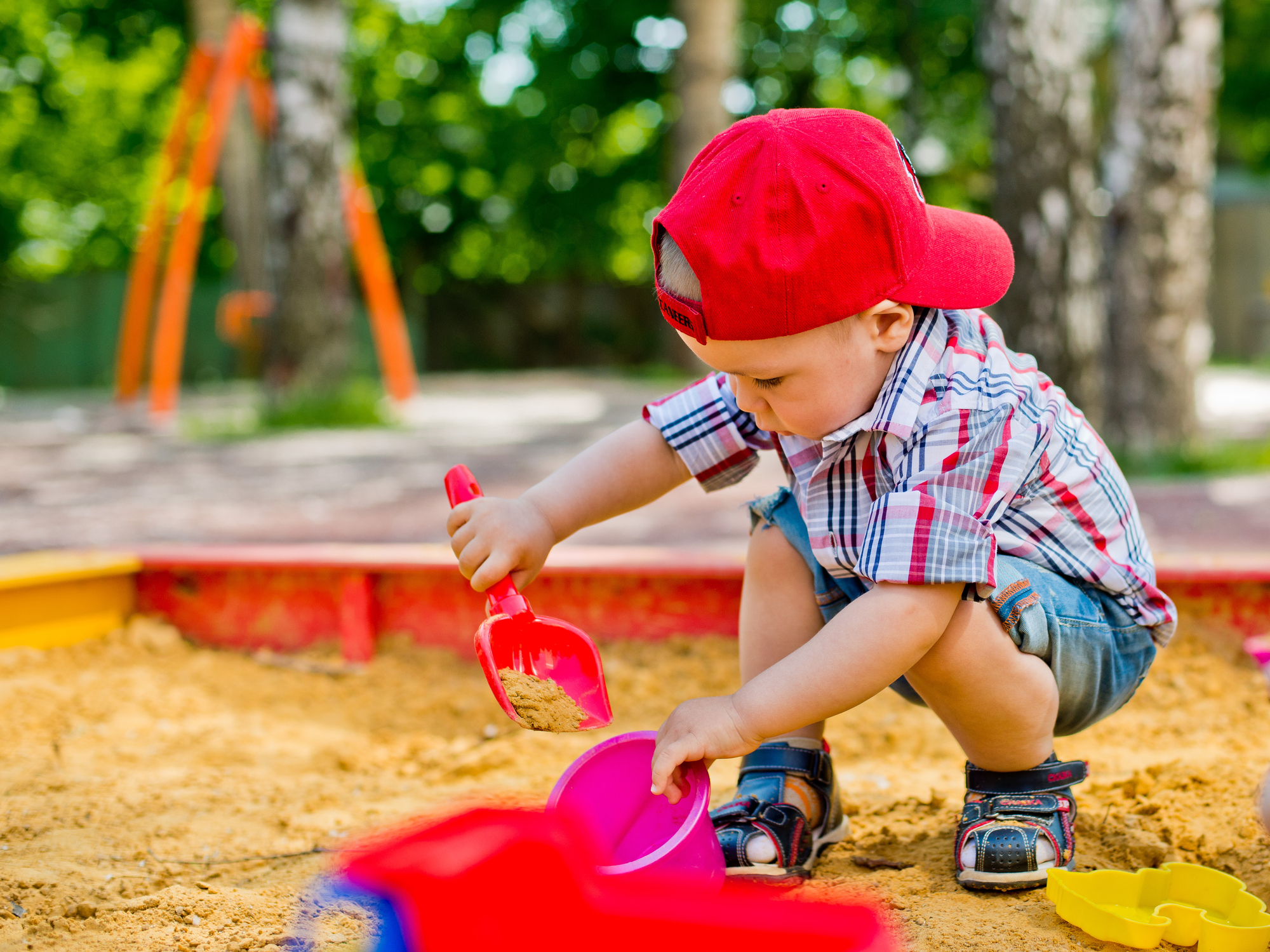 Un bambino che raccoglie la sabbia con una pala in un secchio in una sabbiera.