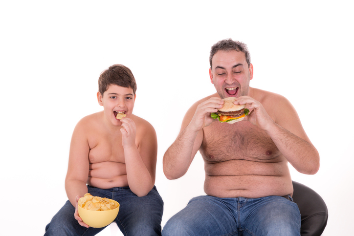 il ragazzo e suo padre mangiano il cibo sbagliato, mangiano hamburger, sono obesi