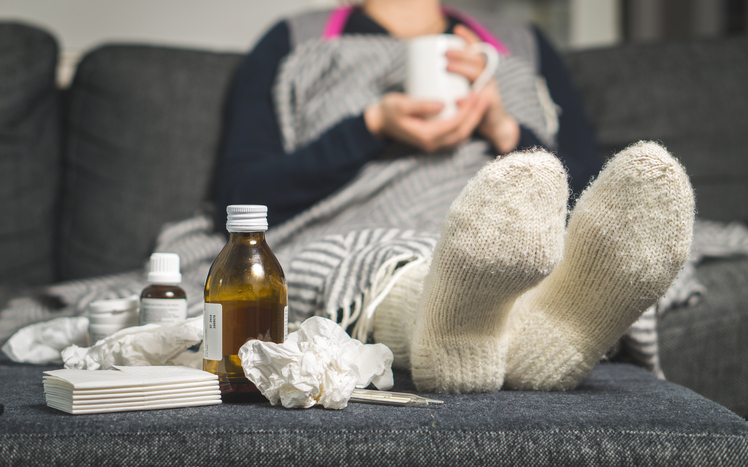 una donna malata è sdraiata a letto con calze calde e pillole e sciroppi accanto a lei