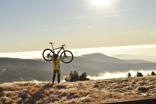 Una ciclista solleva la sua bicicletta sopra la testa. Sullo sfondo, montagne nella nebbia.