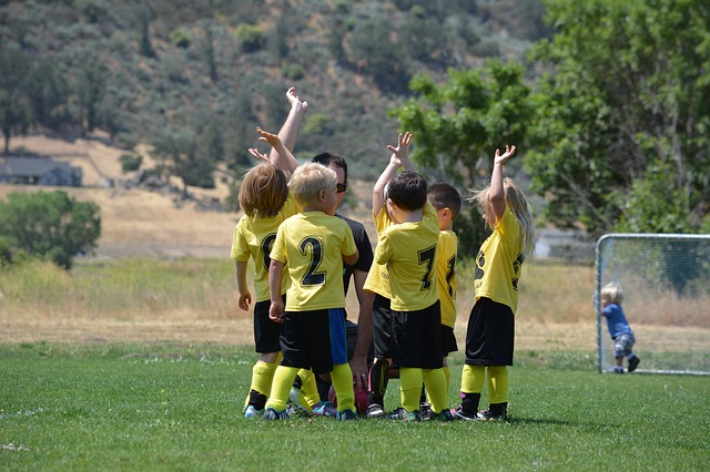 Bambini in maglia gialla sul campo da calcio che si divertono in gruppo con il loro allenatore.