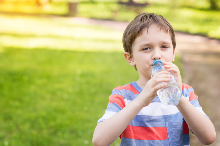 Ragazzo che beve acqua da una bottiglia, sullo sfondo erba verde