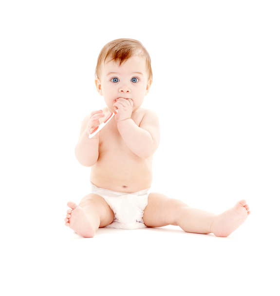 Un bambino piccolo con il pannolino è seduto, con uno spazzolino in mano e in bocca.