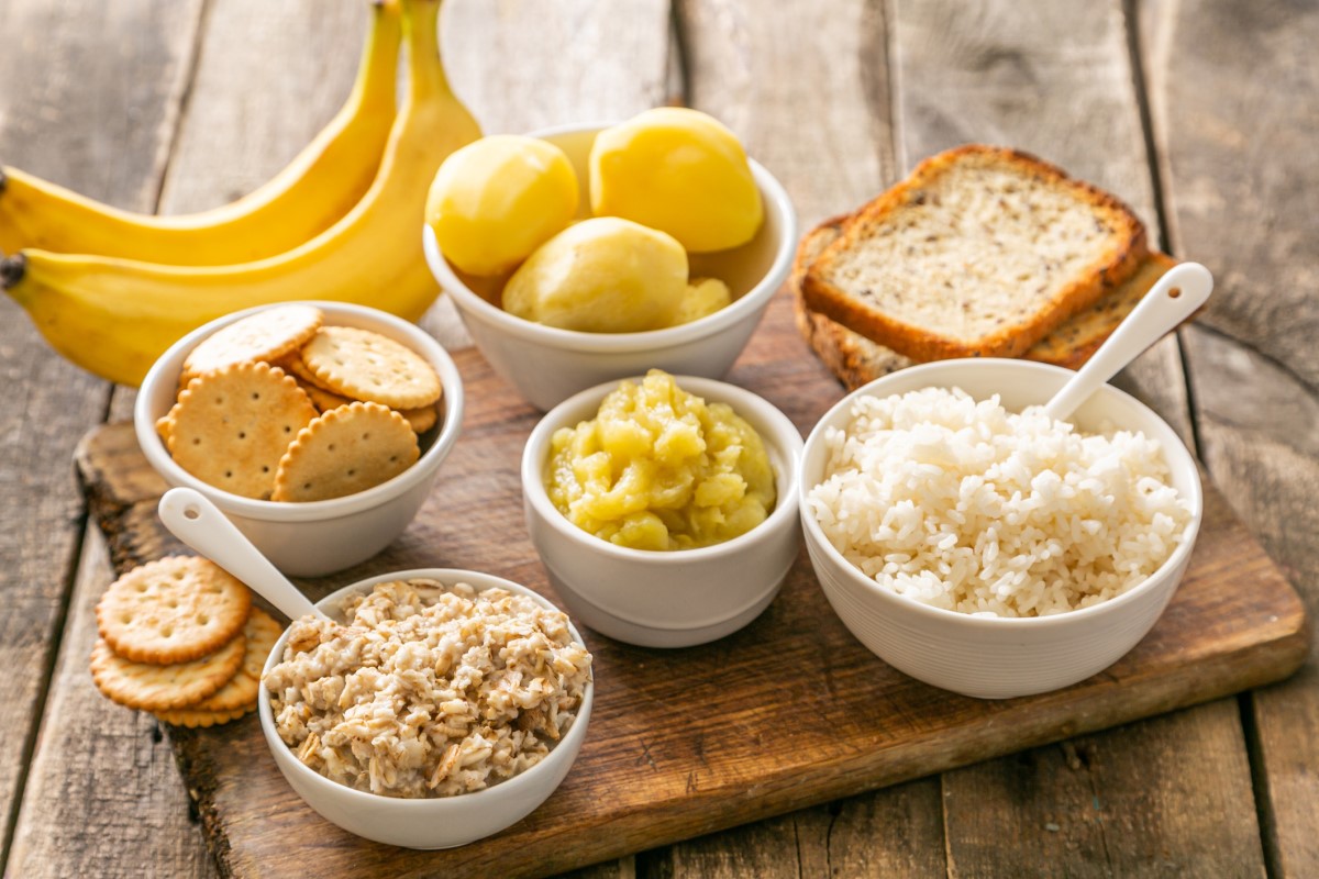 Esempio di dieta appropriata per la diarrea acuta - riso, patate, banane, cracker, gallette, in ciotole e su un tagliere di legno.