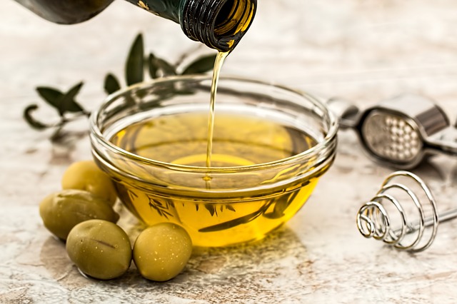 In una ciotola di vetro si versa l'olio d'oliva da una bottiglia di vetro e si dispongono le olive verdi intorno alla ciotola.