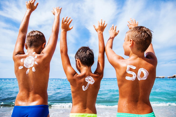 Protezione solare per bambini con OF 50, i bambini sono sulla spiaggia in riva al mare e si divertono, le loro mani sono alzate