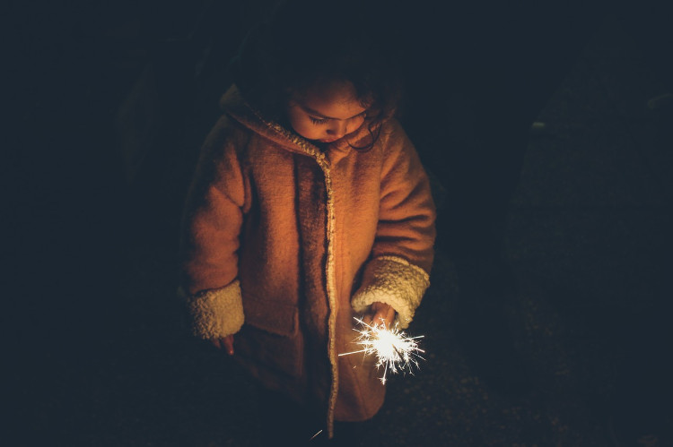 una bambina in cappotto e con una stella filante in mano che guarda tristemente a terra