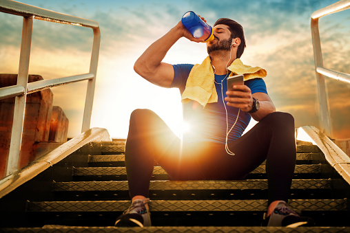 Un atleta seduto sulle scale. Il tramonto. Bere un integratore alimentare da un barattolo.