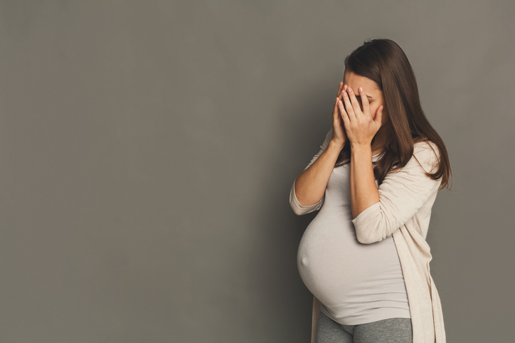 Una donna incinta e stanca che si copre il viso con le mani.