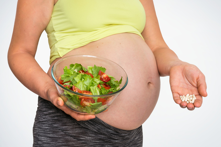 Donna incinta con insalata e pillole