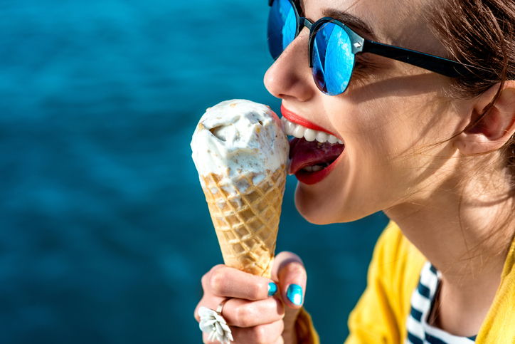 donna con occhiali da sole che lecca un gelato vicino all'acqua