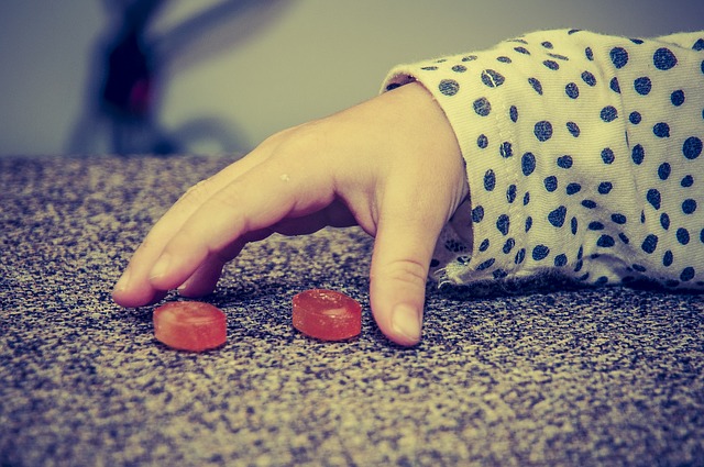 La mano di un bambino, due caramelle rosse, cattive abitudini alimentari