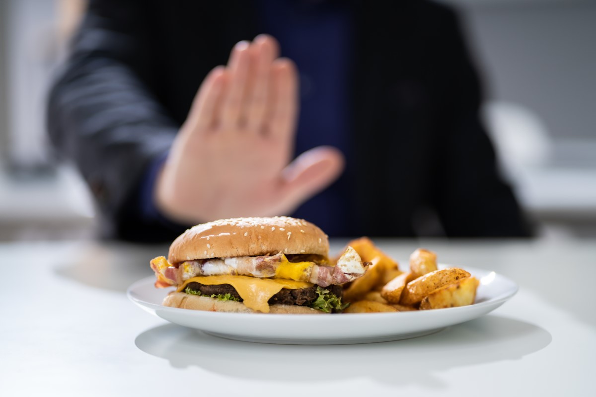 Il cibo inadeguato come causa di bruciore di stomaco: un hamburger su un piatto che un uomo rifiuta