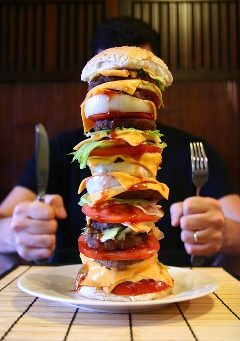 Un uomo siede a un tavolo con un hamburger alto nel piatto, una megaforza