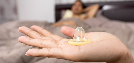 preservativo sulla mano della donna, uomo sdraiato a letto