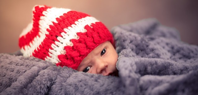 Un bambino, sdraiato e coperto, con un berretto a righe bianche e rosse