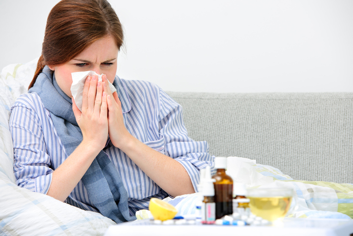 Una donna si pulisce il naso, per un raffreddore, che è la causa di vari disturbi, nella foto ci sono medicine, pillole, bottiglia, spray, limone