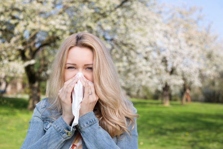 donna con febbre da fieno, starnutisce, è all'aperto, erba e fiori di alberi